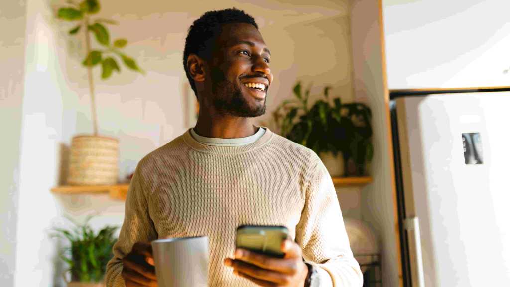 Homem sorri ao encontrar onde investir 5 mil reais em seu smartphone enquanto toma café.