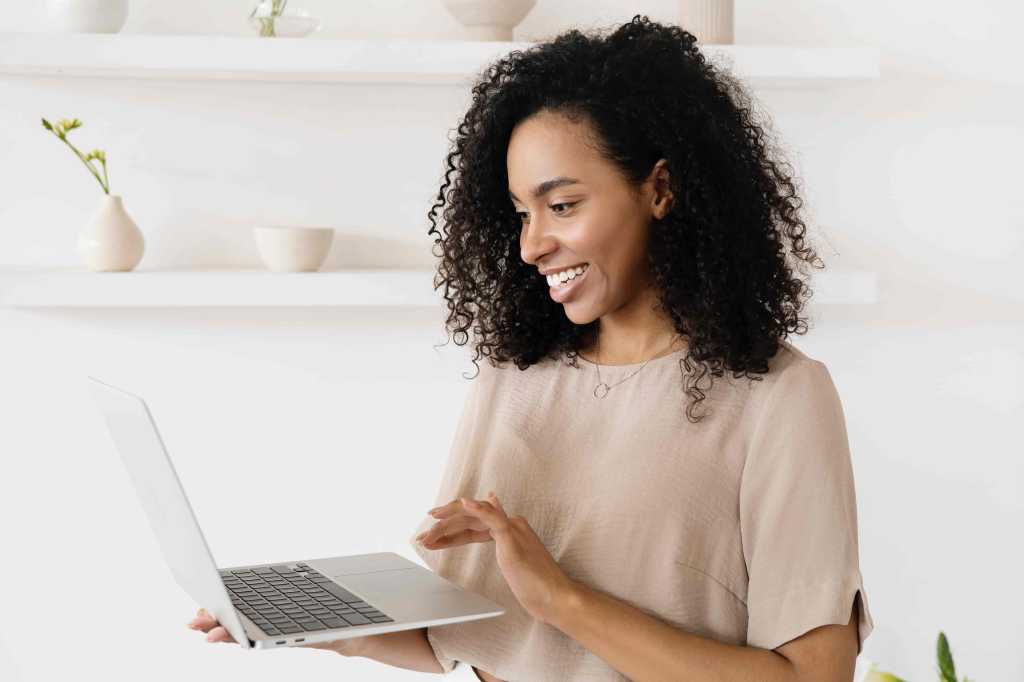 A imagem mostra uma mulher negra com uma notebook na mão em referência à pesquisa sobre a Restituição do Imposto de Renda.