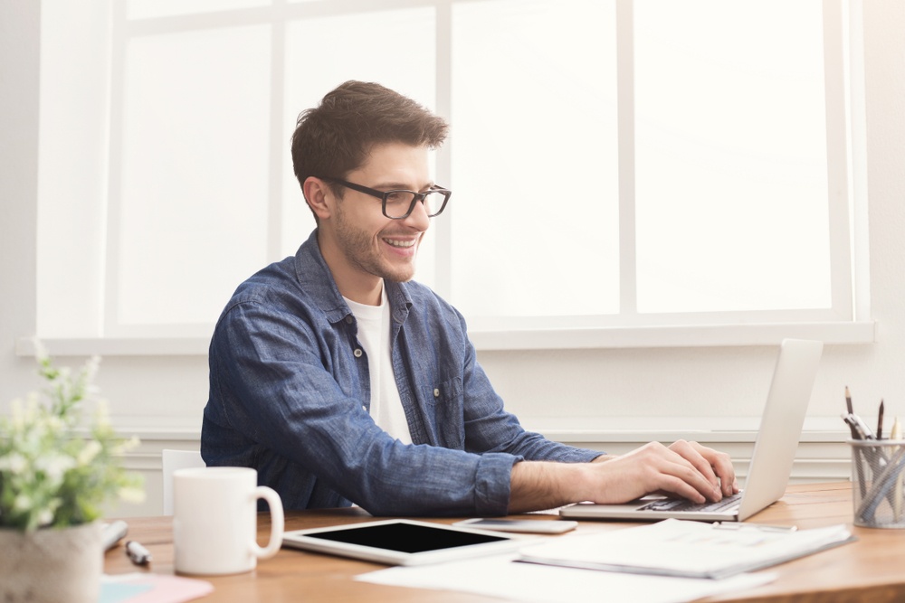 Um homem à mesa de escritório mexendo em um notebook em referência ao tesouro selic simulador