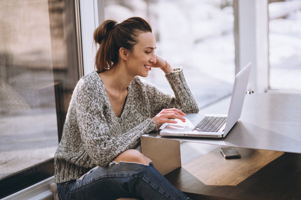 Uma mulher à mesa com o rosto apoiado na mão mexendo no notebook em referência aos títulos de crédito privado