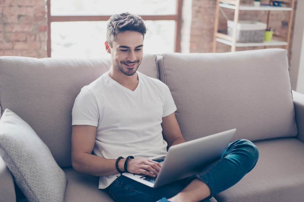 Um homem sentado no sofá com o notebook no colo em referência a vale a pena investir no tesouro direto