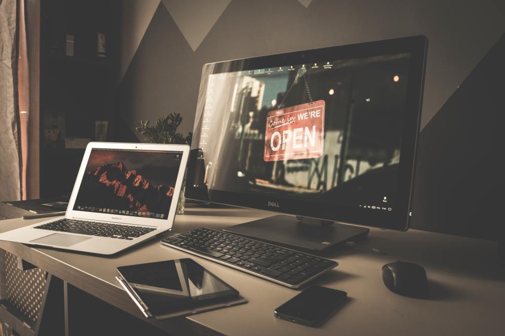 Mesa de escritório com noteboook e monitor com a frase "entre, estamos abertos", em referência ao Open Banking"