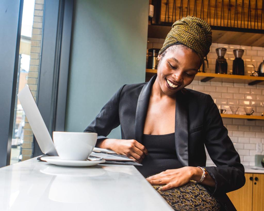 Mulher em um café sentada em frente ao notebook aprendendo sobre a diferença entre ações ordinárias e ações preferenciais.