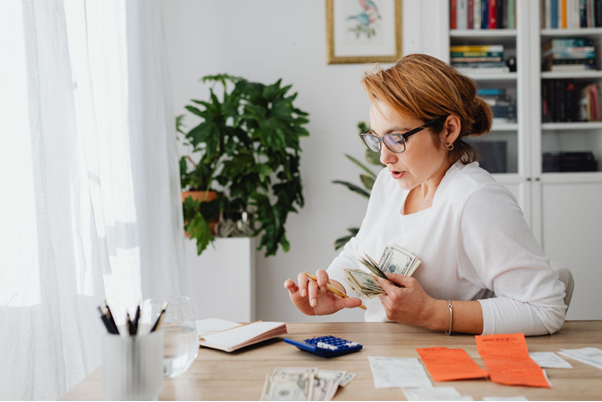 Mulher em frente a uma mesa, com cédulas de dinheiro nas mãos e alguns objetos de escritório a sua frente, procurando entender qual o seu perfil de investidora.