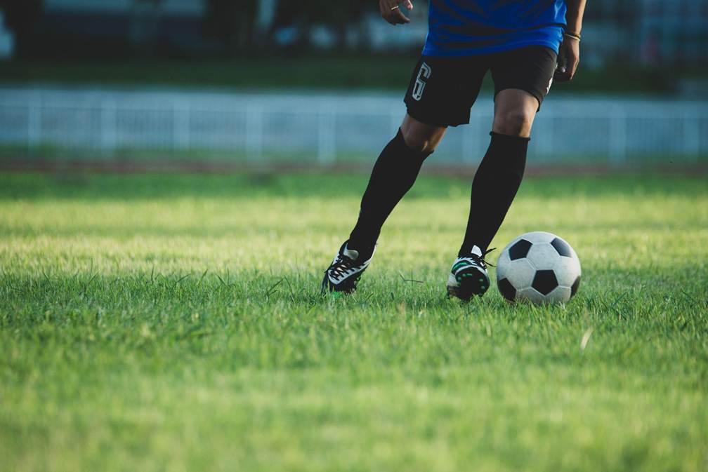 Jogador de futebol conduzindo a bola em campo, representando o tema de como investem os jogadores de futebol fora dos gramados.