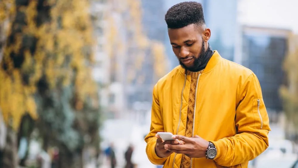 A imagem mostra um homem jovem vestido com um casaco amarelo e uma blusa de gola alta marrom, utilizando um smartphone para conferir o recebimento de um pagamento via Pix.