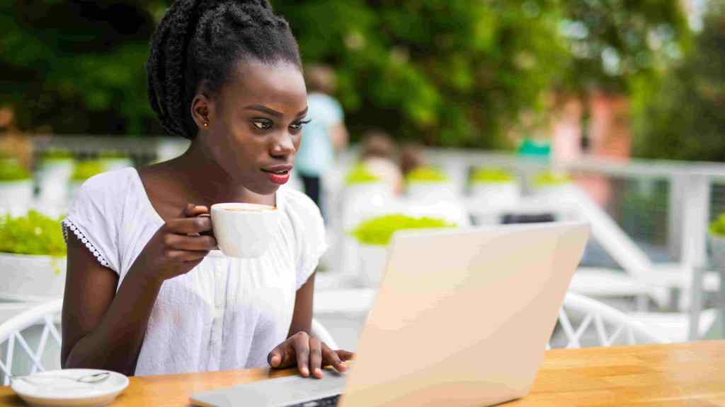 Mulher busca em seu notebook dicas de como economizar dinheiro enquanto toma um café.