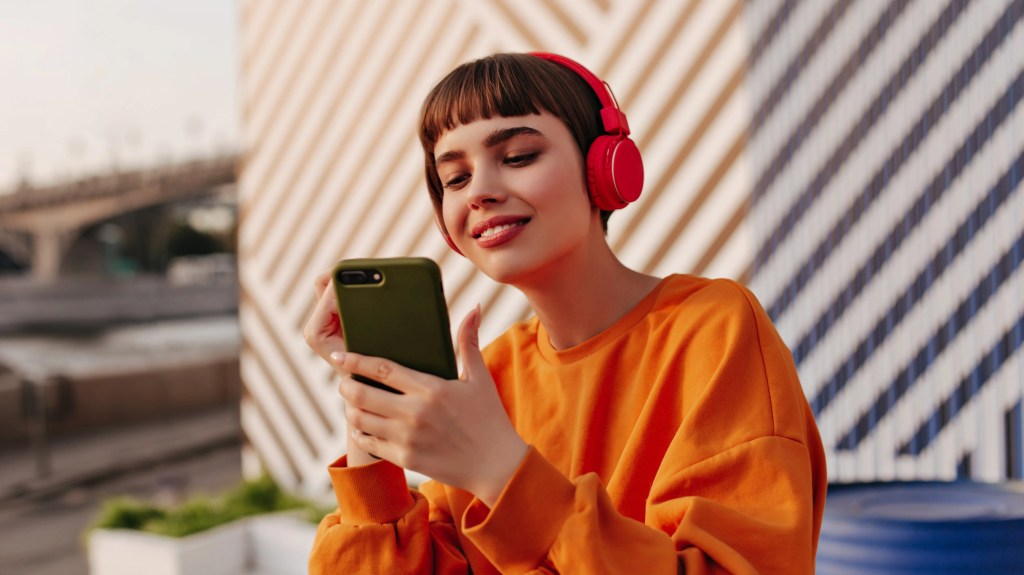 Jovem usando fones de ouvido busca pelo ranking de artistas mais ricos em seu smartphone.