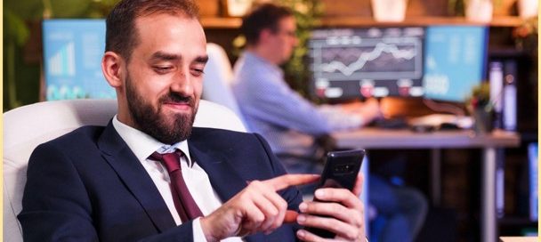Homem de terno e gravata sorri ao acompanhar seus investimentos em treasuries pelo celular. O cenário de fundo mostra um ambiente profissional com foco em análise de dados financeiros.