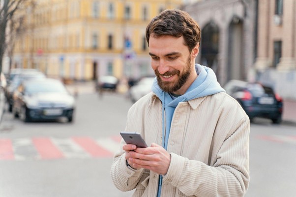 Homem sorrindo digitando em um celular enquanto caminha na rua.