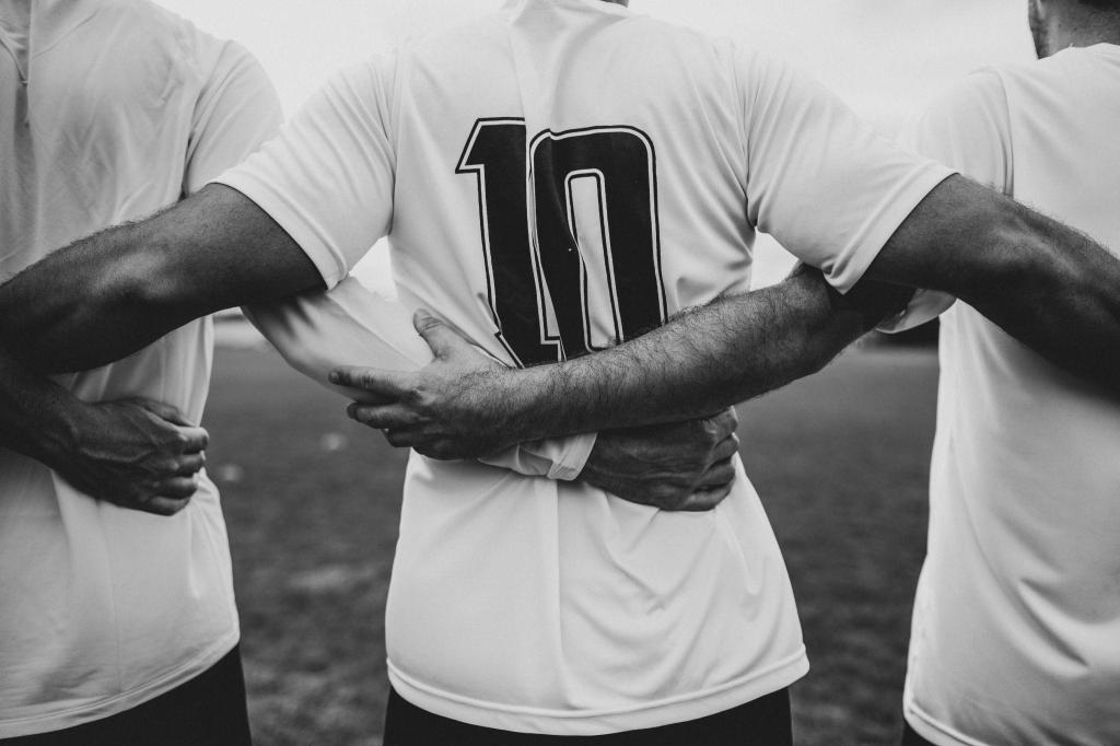 Vista aproximada das costas de três jogadores de futebol abraçados, com o atleta central vestindo uma camisa branca de número 10.