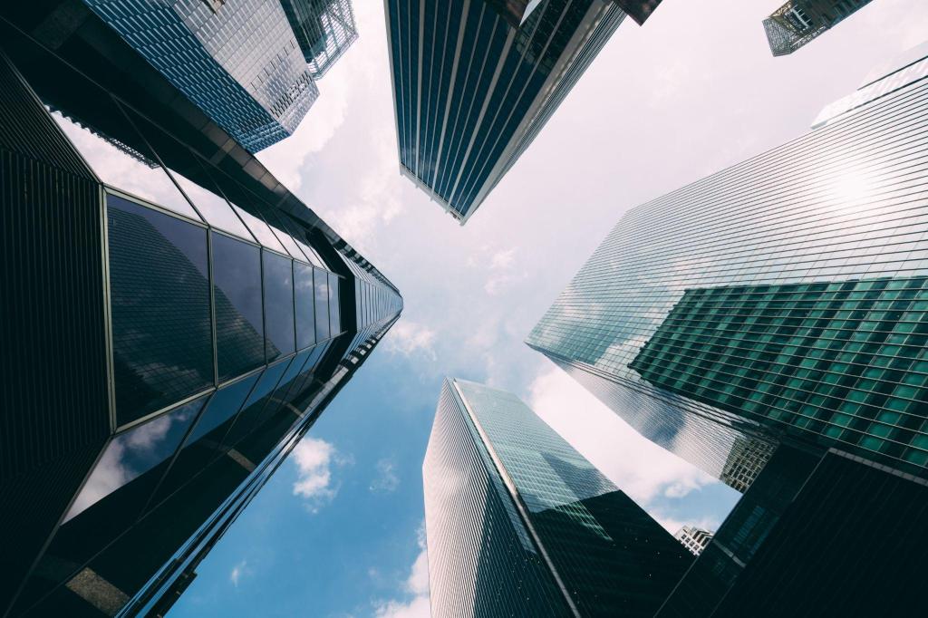 Vista de baixo de arranha-céus modernos e prédios comerciais espelhados sob um céu claro, representando o mercado imobiliário corporativo investido por REITs americanos.