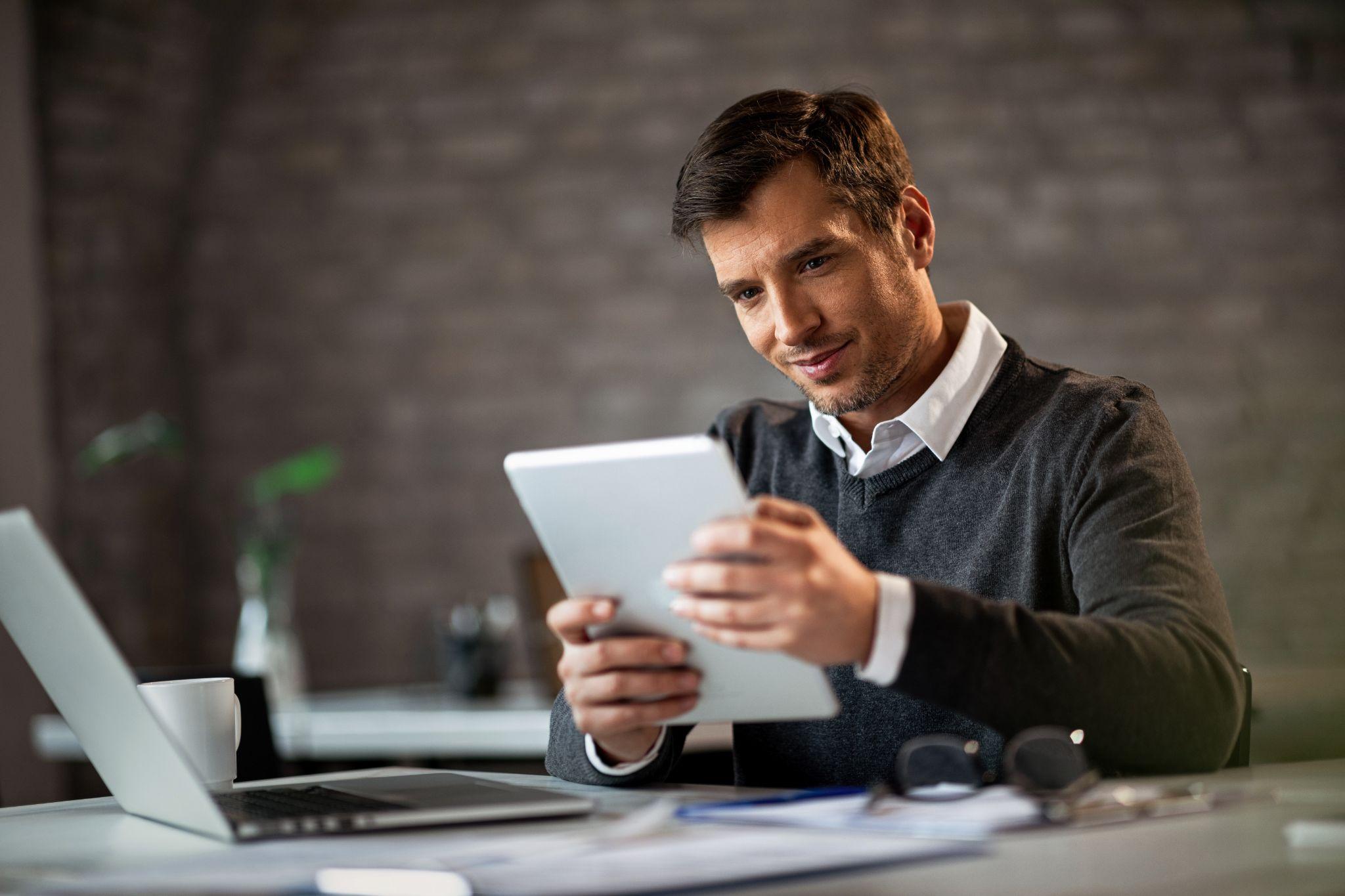Jovem investidor sorrindo em um escritório moderno enquanto mexe em um tablet, ilustrando a facilidade de gerenciar e aplicar em CDs pela Rico.