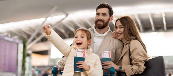 Família feliz com criança pequena no aeroporto, segurando passagens e malas, representando o início de uma viagem planejada e segura com o Seguro Viagem Rico.